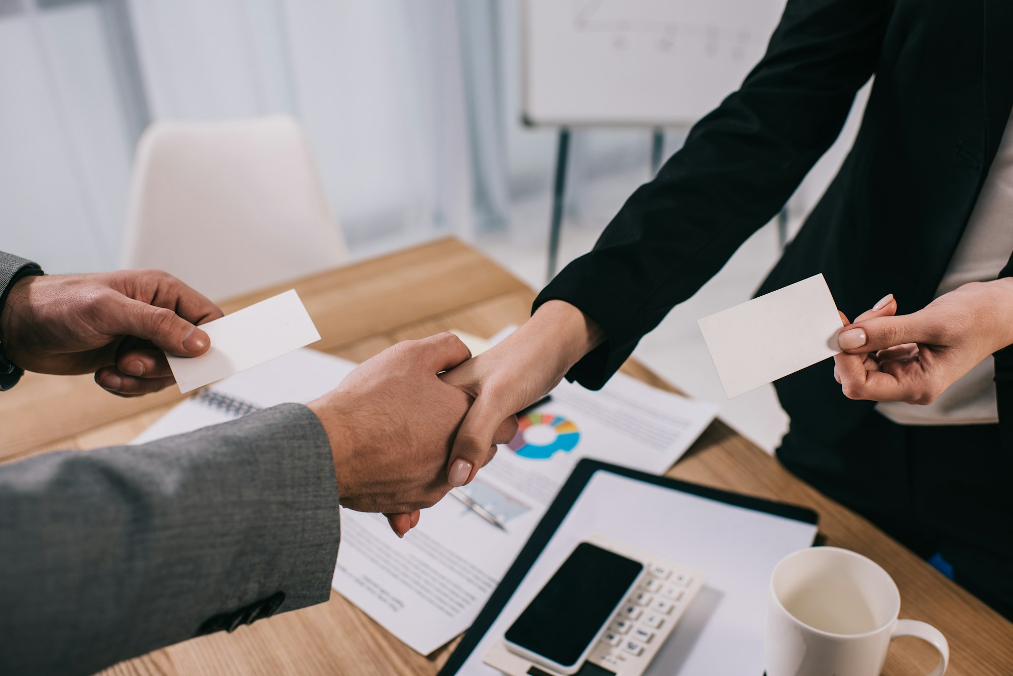 Cropped view of business partners shaking hands and giving visit cards to each other