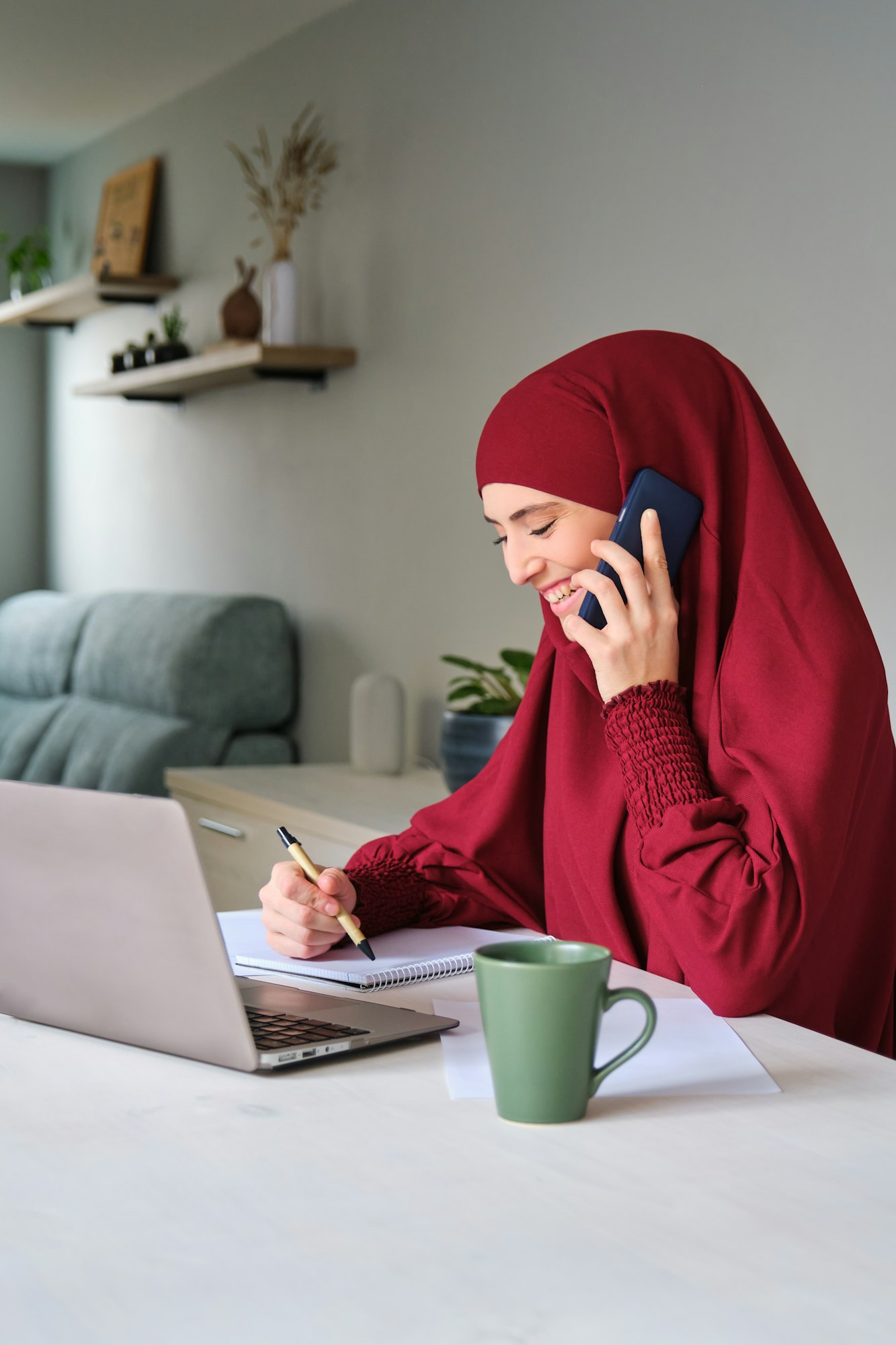 Muslim young woman student in hijab laughing in a phone call while studying.